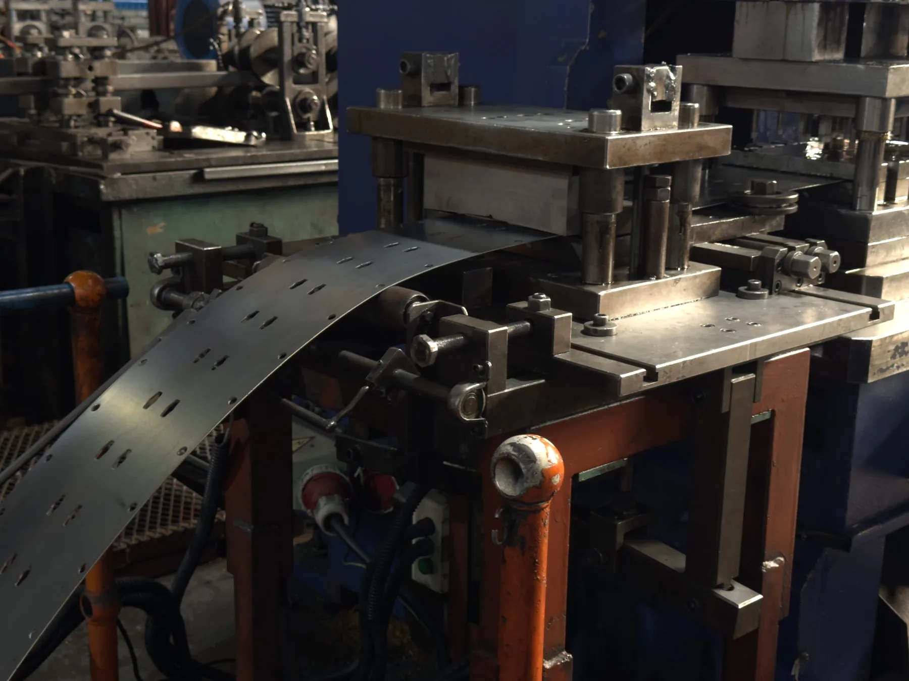 Perforated strip advancing through industrial press tooling
